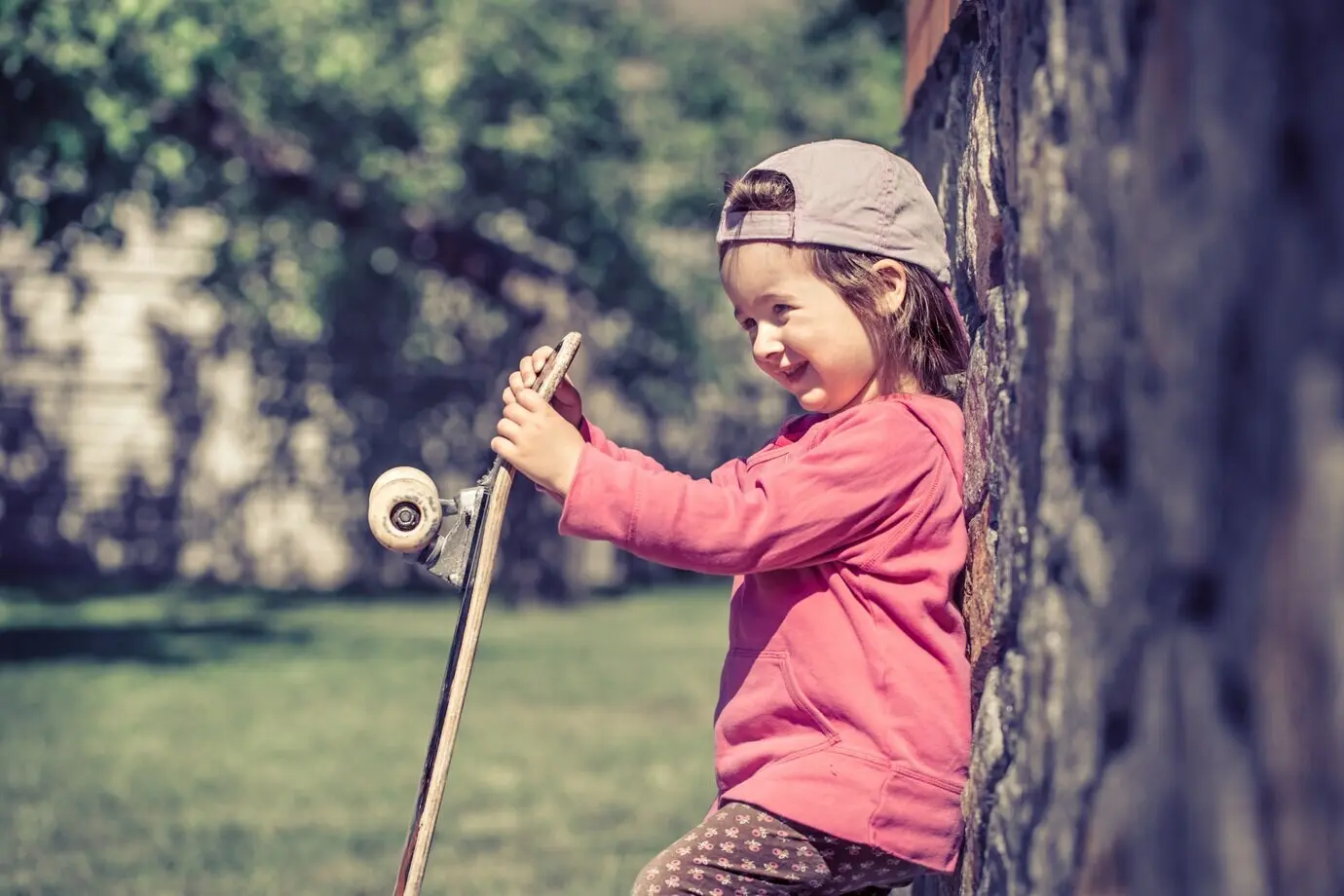 Ein modisch gekleidetes kleines Mädchen hält ein Skateboard und spielt im Freien – die schönen Gefühle eines Kindes.
